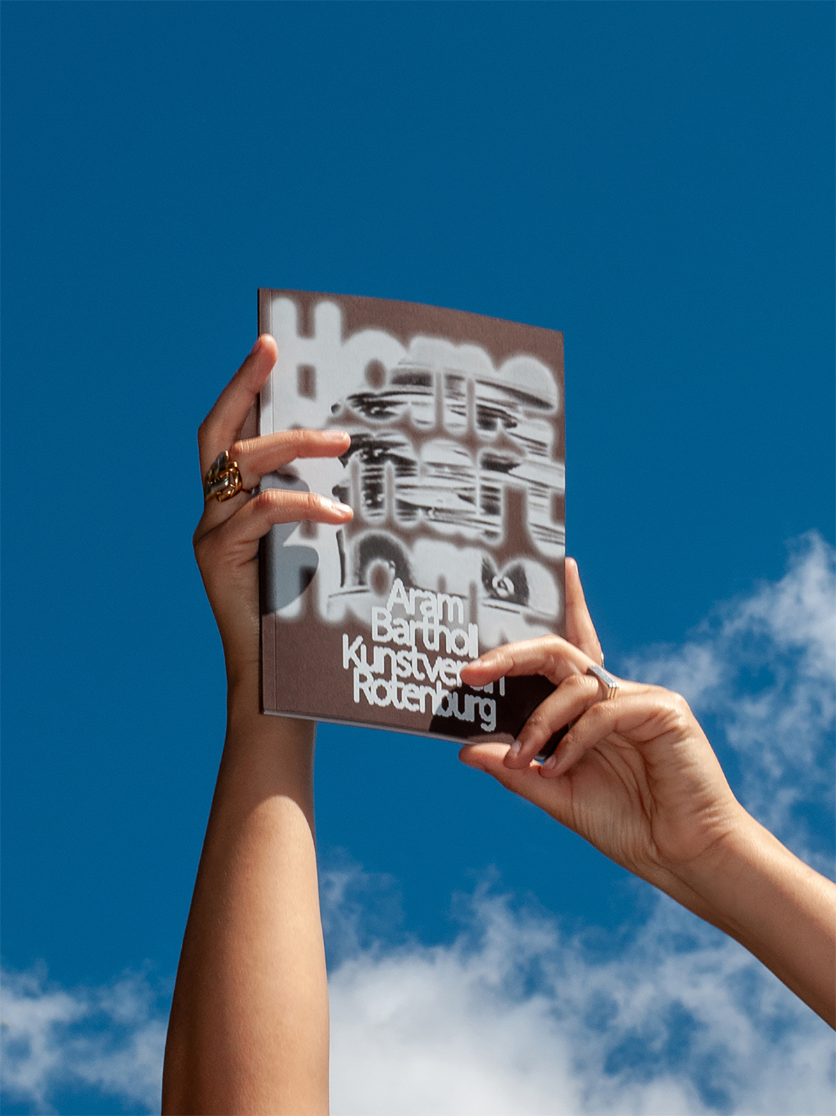 Zwei Hände halten ein Buch vor blauem Himmel; Cover mit unscharf überlagerter Typografie und Titel »Aram Bartholl Kunstverein Roterburg« in Weiß.