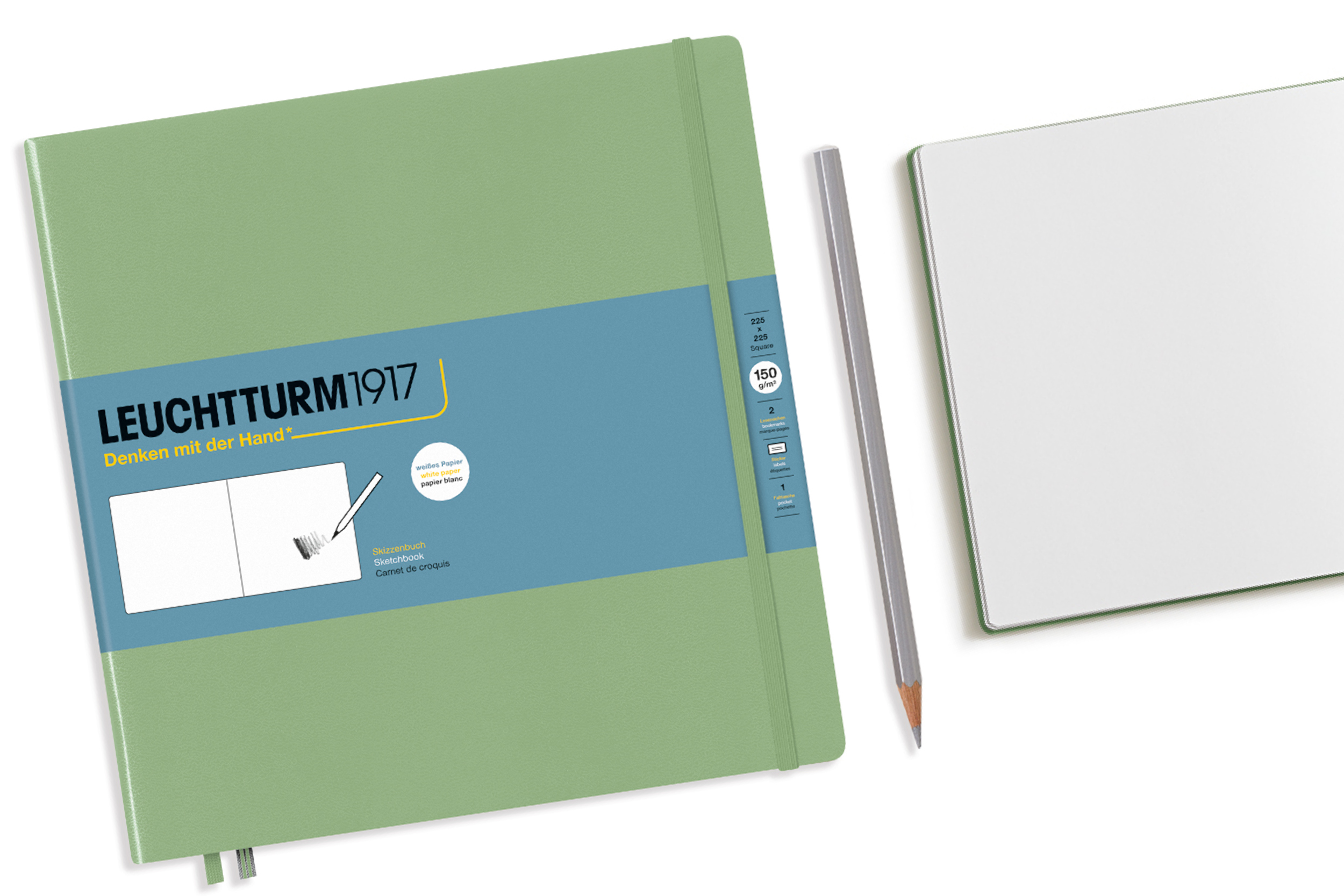 Grünes Skizzenbuch „Leuchtturm1917 – Denken mit der Hand“ mit blauem Banderolenlabel; daneben liegt ein Bleistift und ein geöffnetes Notizbuch mit leeren Seiten auf hellem Hintergrund.