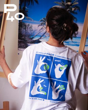 Person von hinten vor einem tropischen Strandposter, trägt ein weißes T-Shirt mit blauem, vierteiligem Comic-Motiv: Hände formen eine Erde und den Schriftzug „You shape the world. Do it with love!“ sowie „40 years of PAGE. Celebrating design.“