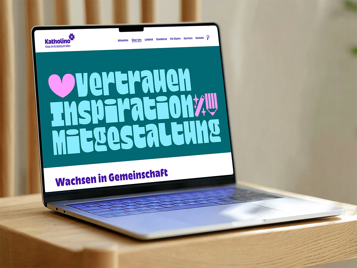 Website-Mockup von Katholino – Kitas im Erzbistum Köln, dargestellt auf einem Laptop auf einem Holztisch. Der Bildschirm zeigt den Hero-Bereich mit den drei Leitworten »Vertrauen, Inspiration, Mitgestaltung« in großer, fetter Türkisschrift auf dunkelgrünem Hintergrund, ergänzt durch pinke Illustrationen. Darunter steht der Claim »Wachsen in Gemeinschaft« in kräftigem Violett.
