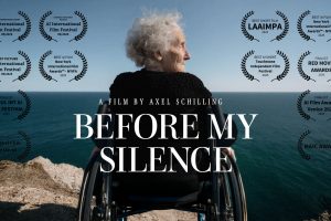 Filmplakat zu „Before My Silence“ von Axel Schilling: Im Zentrum sitzt eine ältere Person mit weißem Haar in einem Rollstuhl auf einer Felsklippe und blickt aufs offene Meer. Die Szene ist von hinten aufgenommen und vermittelt eine ruhige, nachdenkliche Atmosphäre mit weitem Horizont und blauem Himmel. Über dem Bild steht „A Film by Axel Schilling“, darunter groß der Filmtitel „Before My Silence“. Rund um das Motiv sind zahlreiche Festival-Auszeichnungen und Lorbeerkränze angeordnet, darunter Preise und Nominierungen internationaler KI- und Kurzfilmfestivals. Die Gestaltung vermittelt eine emotionale, cineastische Stimmung zwischen Einsamkeit, Erinnerung und Reflexion.