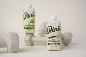 Pinu High Protein Drink in cremefarbenem Packaging mit Pistazie oder Vanilleschote Illustration und auf Hanteln dekoriert