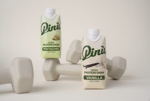 Pinu High Protein Drink in cremefarbenem Packaging mit Pistazie oder Vanilleschote Illustration und auf Hanteln dekoriert