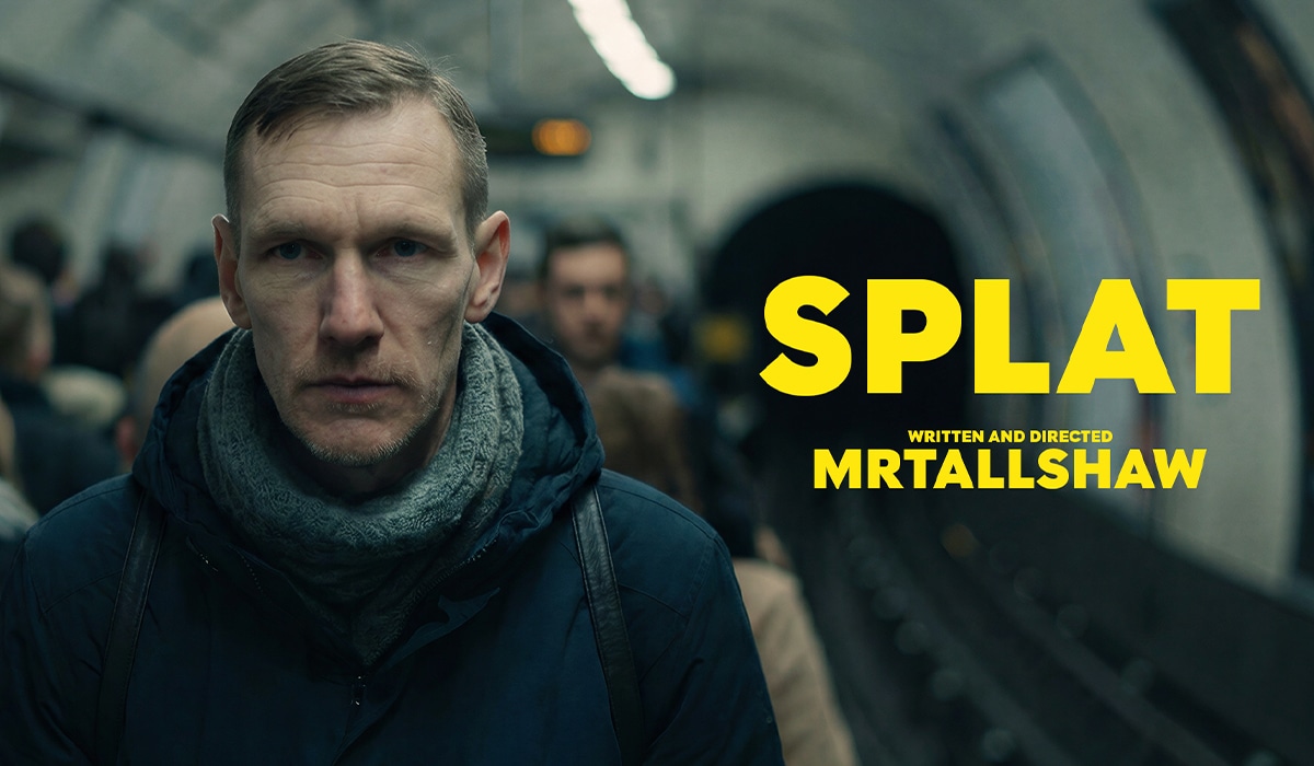 Filmplakat mit einem ernst blickenden Mann in dunkler Jacke und grauem Schal auf einem belebten U-Bahnsteig. Im Hintergrund verschwimmen wartende Menschen und ein Tunnel. Rechts steht in leuchtend gelber Schrift der Titel „SPLAT“, darunter „Written and Directed MRTALLSHAW“.