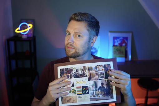 Mann hält eine Präsentationstafel mit Moodboard und Branding-Entwürfen für „Soléa“ in die Kamera; im Hintergrund ein farbig beleuchteter Raum.