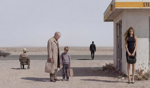 Surreal inszenierte Szene an einer verlassenen Tankstelle in einer kargen Wüstenlandschaft. Ein älterer Mann und ein Junge stehen mit Einkaufstüten im Vordergrund, während eine junge Frau im schwarzen Kleid an der Gebäudewand lehnt. Im Hintergrund sitzen und gehen zwei weitere Männer an einer einsamen Straße.