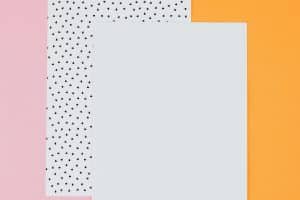Ein weißes und ein mit schwarzen Punkten markiertes Blätter Papier, vor einem organge- und pinkfarbenen Hintergrund, Stil ist poppig-heiter