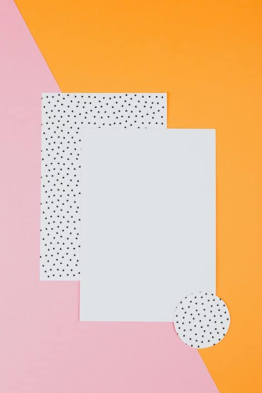 Ein weißes und ein mit schwarzen Punkten markiertes Blätter Papier, vor einem organge- und pinkfarbenen Hintergrund, Stil ist poppig-heiter